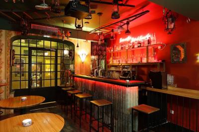 Intérieur d'un bar avec comptoir en métal, éclairage rouge, tables en bois et décorations murales éclectiques.