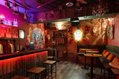 Intérieur d'un bar avec comptoir en métal, éclairage rouge, tables en bois et décorations murales éclectiques.