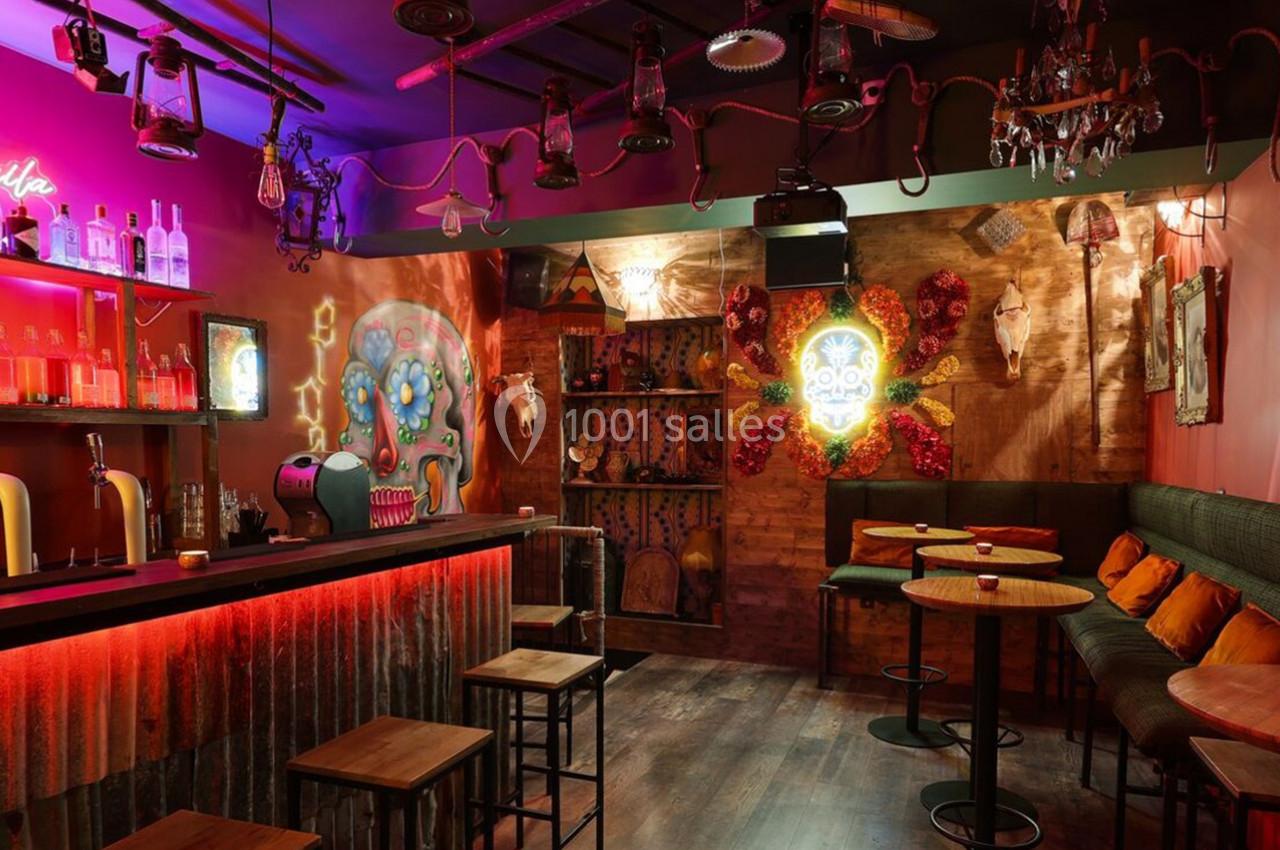 Bar à l'ambiance mexicaine avec éclairage tamisé, décorations colorées et tables hautes en bois.