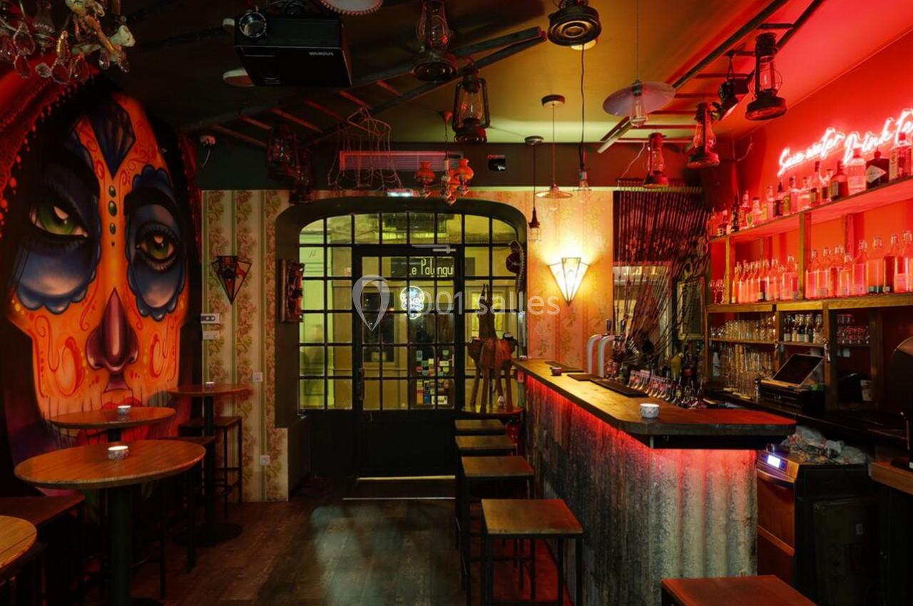 Bar à l'ambiance tamisée avec un mur décoré d'une fresque colorée et un éclairage rouge néon au-dessus du comptoir.