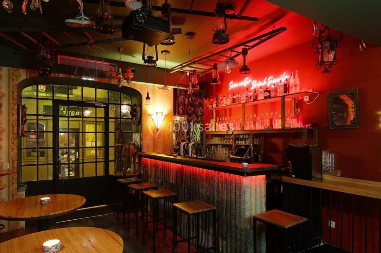 Bar à l'ambiance chaleureuse avec comptoir éclairé, tables en bois et décorations murales éclectiques.