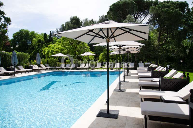 Piscine extérieure entourée de chaises longues et de parasols, située dans un cadre verdoyant.