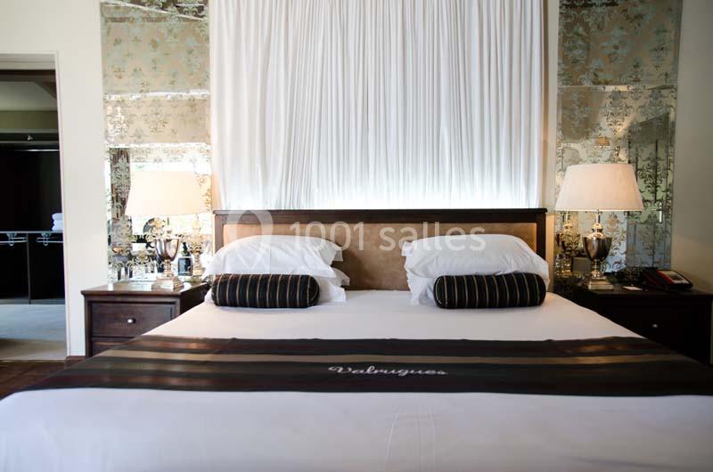 Lit double avec draps blancs, coussins rayés, deux lampes de chevet et un décor mural réfléchissant.