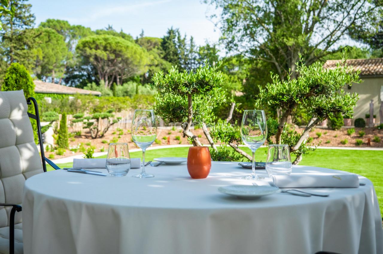 Table dressée en extérieur avec nappes blanches, verres et une vue sur un jardin arboré par une journée ensoleillée.