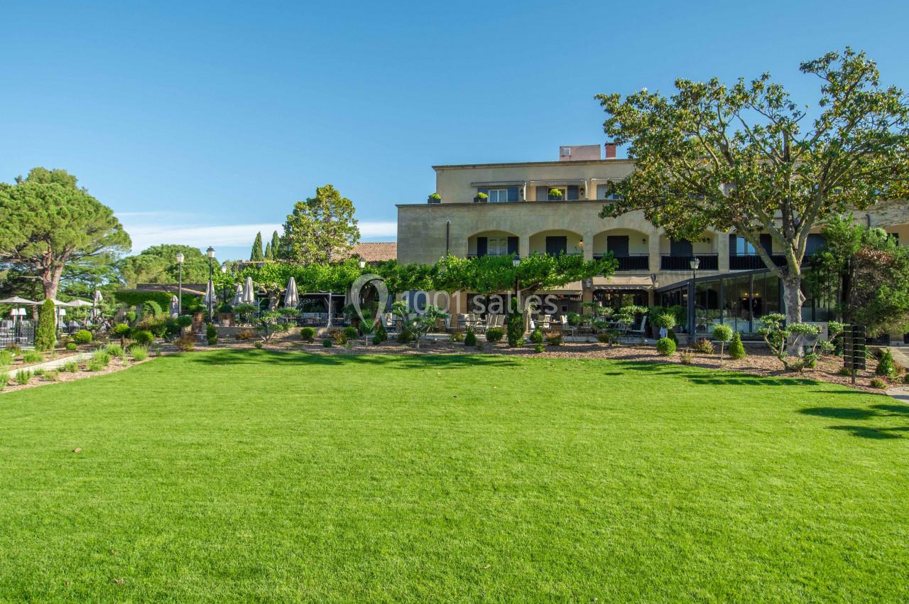 Pelouse verdoyante devant un bâtiment avec terrasses ombragées et arbres sous un ciel dégagé.