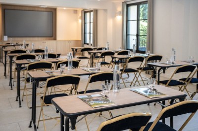 Salle de réunion lumineuse avec des tables disposées en U, des chaises noires et des fenêtres donnant sur un espace vert.