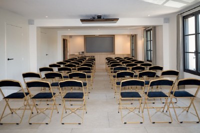 Salle de réunion lumineuse avec des tables disposées en U, des chaises noires et des fenêtres donnant sur un espace vert.