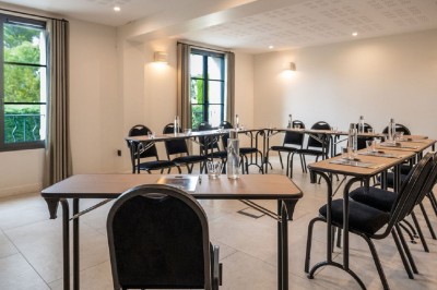 Salle de réunion lumineuse avec des tables disposées en U, des chaises noires et des fenêtres donnant sur un espace vert.