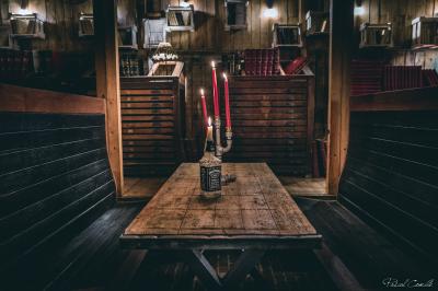 Un chandelier allumé éclaire des livres anciens posés sur un pupitre en bois, devant une fresque sombre et colorée.