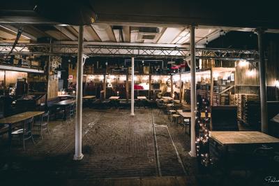 Un chandelier allumé éclaire des livres anciens posés sur un pupitre en bois, devant une fresque sombre et colorée.