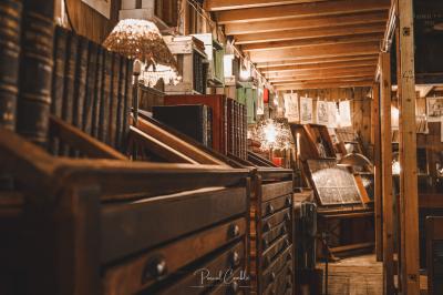 Un chandelier allumé éclaire des livres anciens posés sur un pupitre en bois, devant une fresque sombre et colorée.