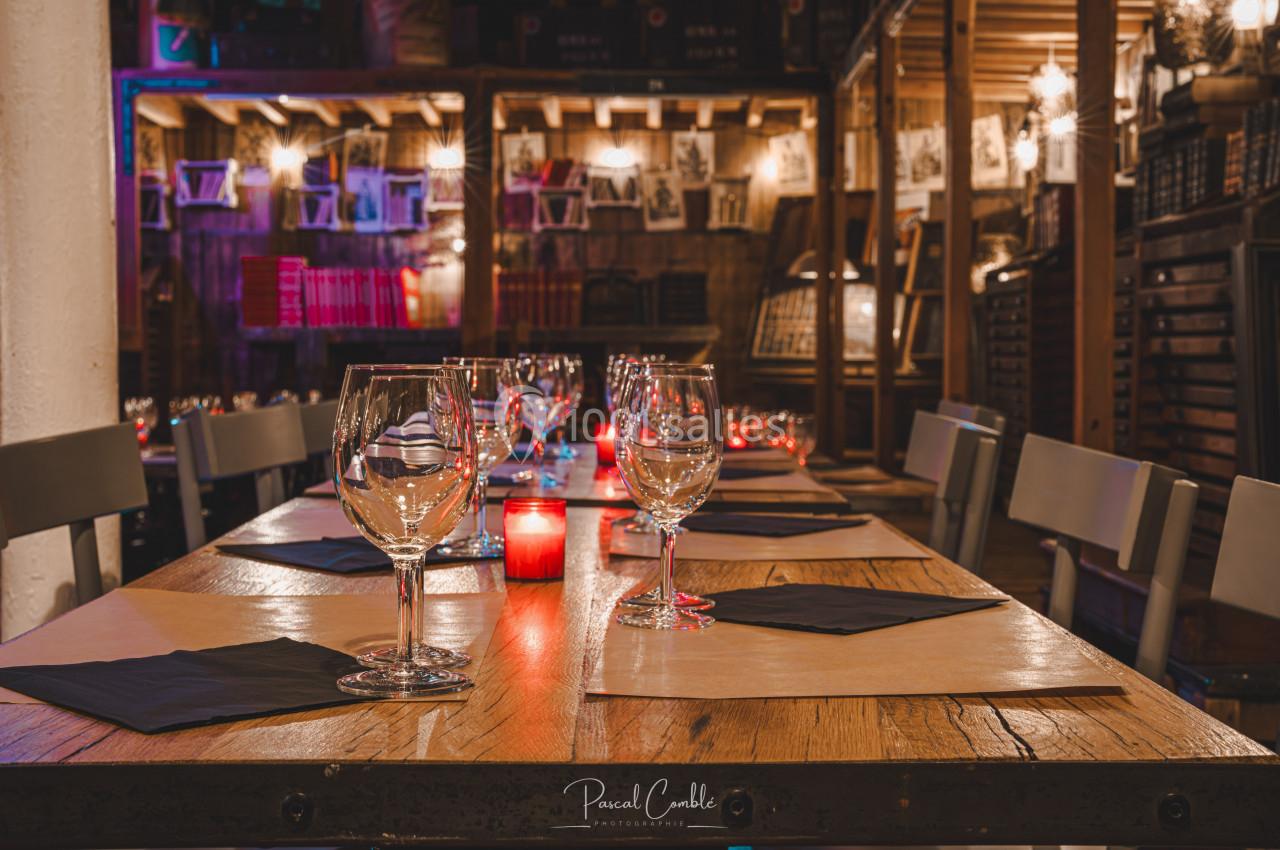 Table en bois dressée avec des verres, serviettes noires et bougies rouges dans une ambiance chaleureuse et tamisée.