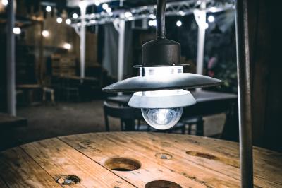 Un chandelier allumé éclaire des livres anciens posés sur un pupitre en bois, devant une fresque sombre et colorée.