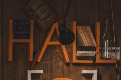 Un chandelier allumé éclaire des livres anciens posés sur un pupitre en bois, devant une fresque sombre et colorée.