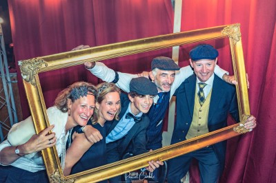 Cinq personnes souriantes posant ensemble derrière un grand cadre doré, devant un fond de rideaux rouges.