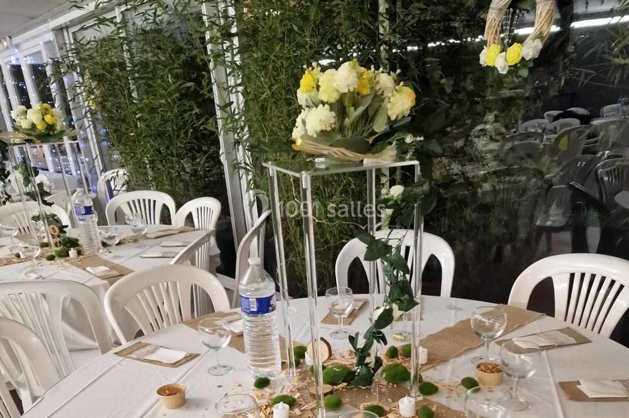 Tables décorées pour un événement, avec nappes blanches, centres de table floraux et chaises en plastique blanc.