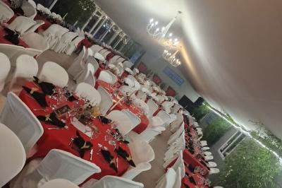 Deux tables rondes décorées pour un événement, avec nappes blanches, fleurs, verres et serviettes pliées.