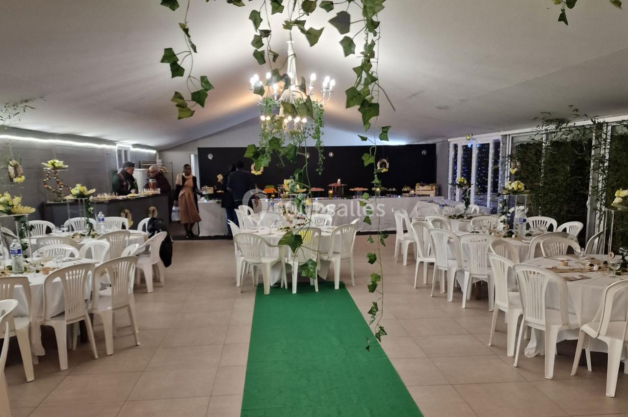 Salle de réception décorée avec des plantes suspendues, tables dressées et buffet au fond.