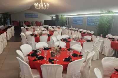 Deux tables rondes décorées pour un événement, avec nappes blanches, fleurs, verres et serviettes pliées.