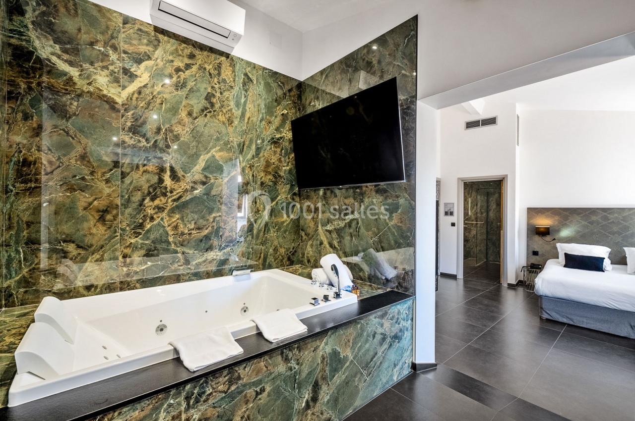 Salle de bain moderne avec baignoire à remous encastrée dans un revêtement en marbre vert, vue sur une chambre adjacente.