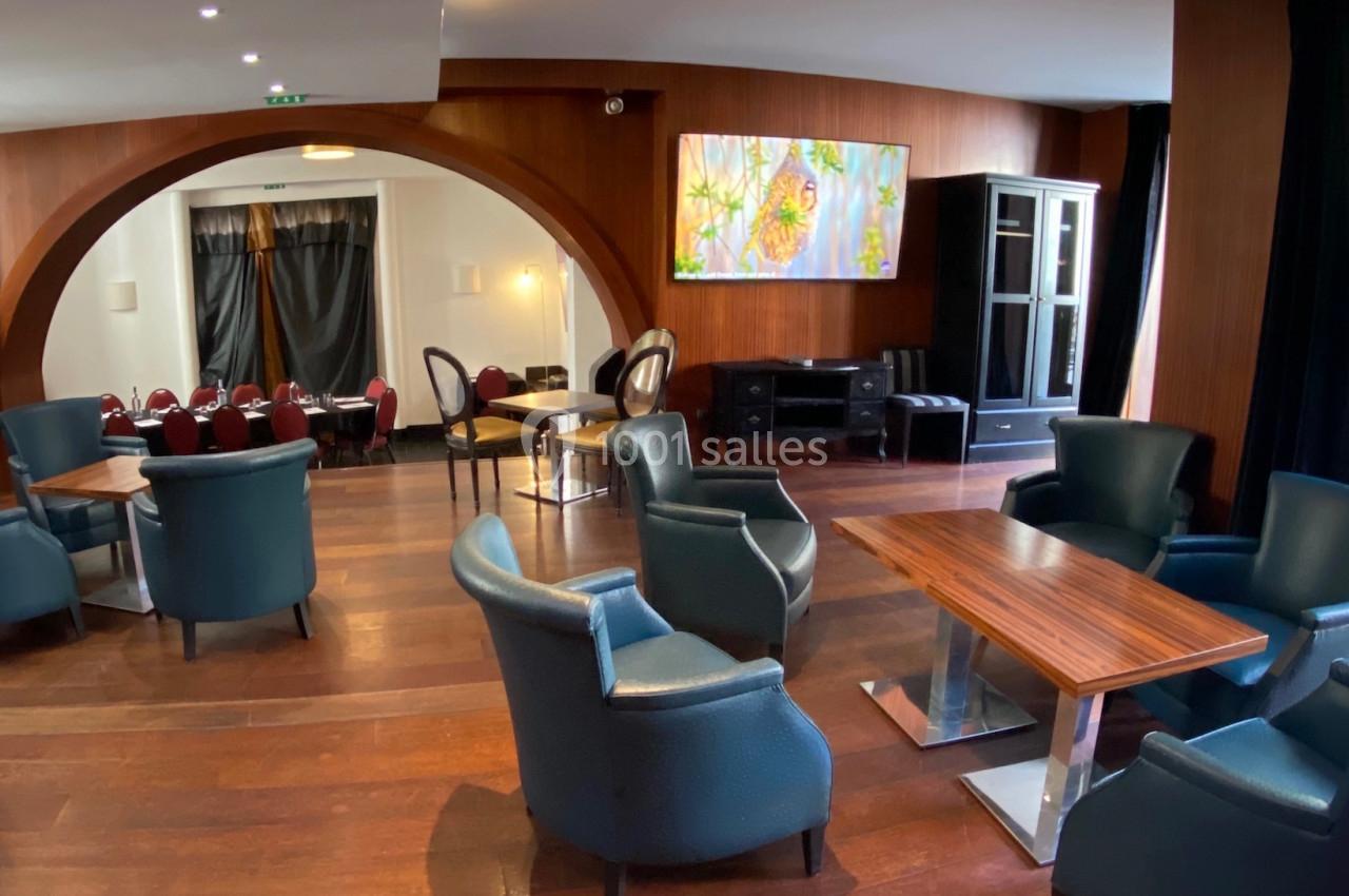 Salle avec fauteuils en cuir, tables en bois, grande arche, tableau coloré et lumière naturelle provenant d'une baie vitrée.