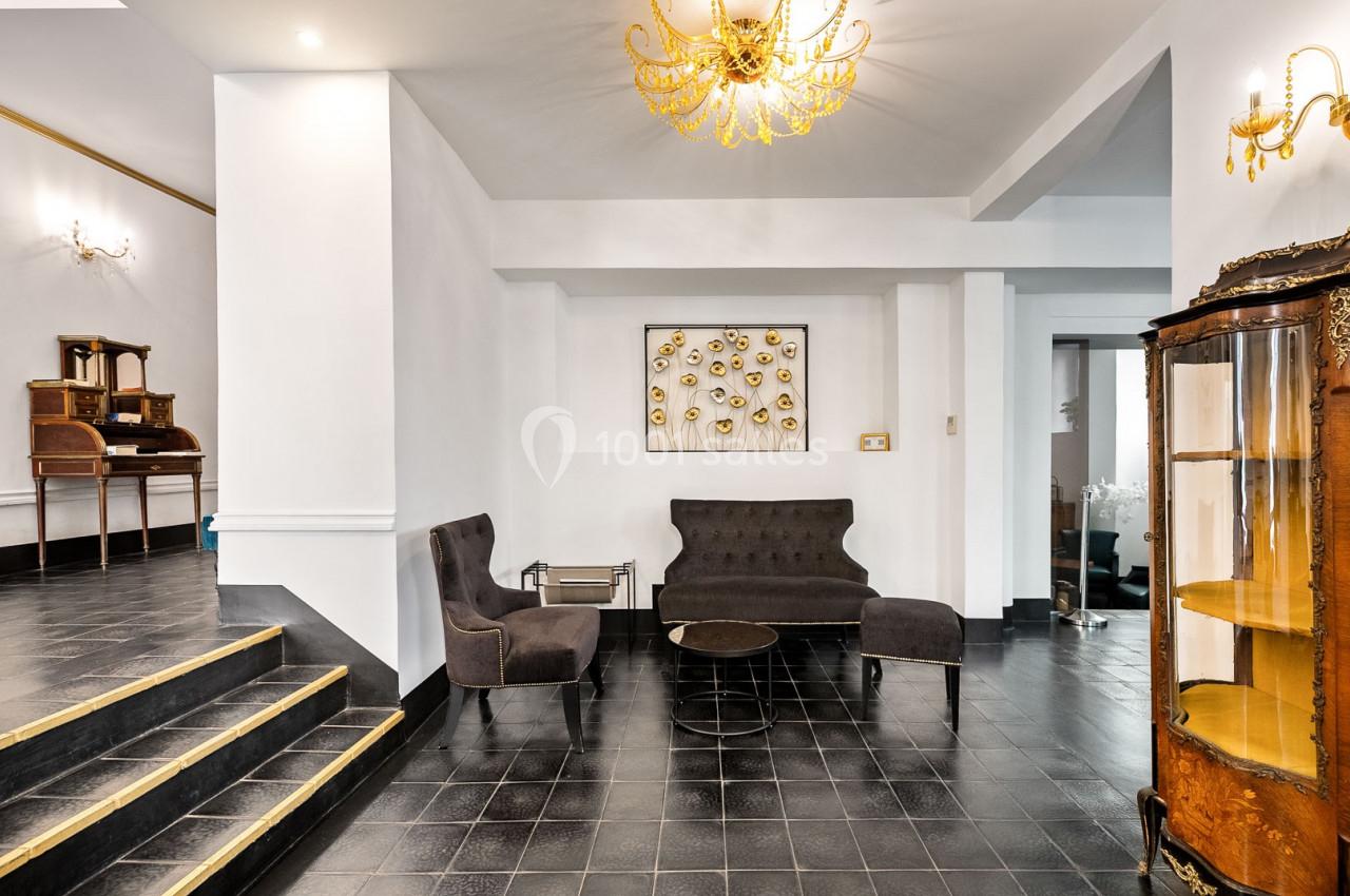 Salon élégant avec fauteuils noirs, table basse ronde, sol en carrelage noir et lustres dorés dans un intérieur lumineux.