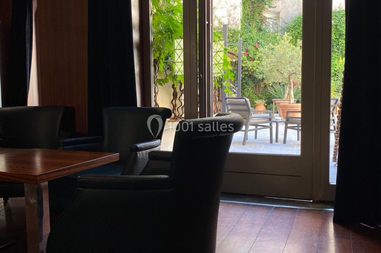Espace intérieur avec fauteuils sombres près d'une porte vitrée donnant sur une terrasse verdoyante.