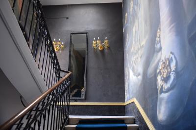 Escalier intérieur avec rampe en fer forgé, miroir mural, appliques dorées et fresque artistique sur le mur.