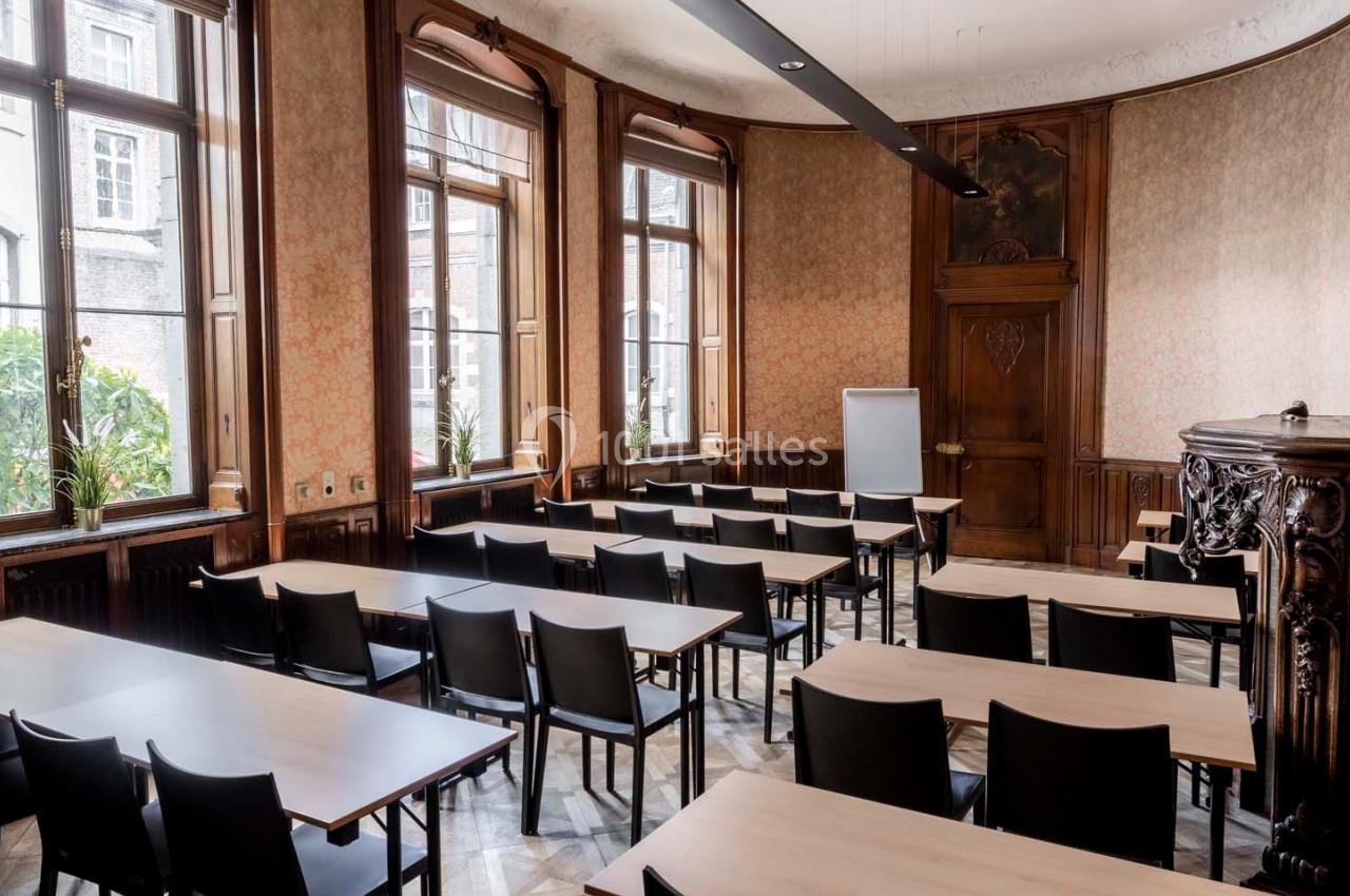 Salle de réunion lumineuse avec des tables en bois clair, des chaises noires et un tableau blanc devant des fenêtres.