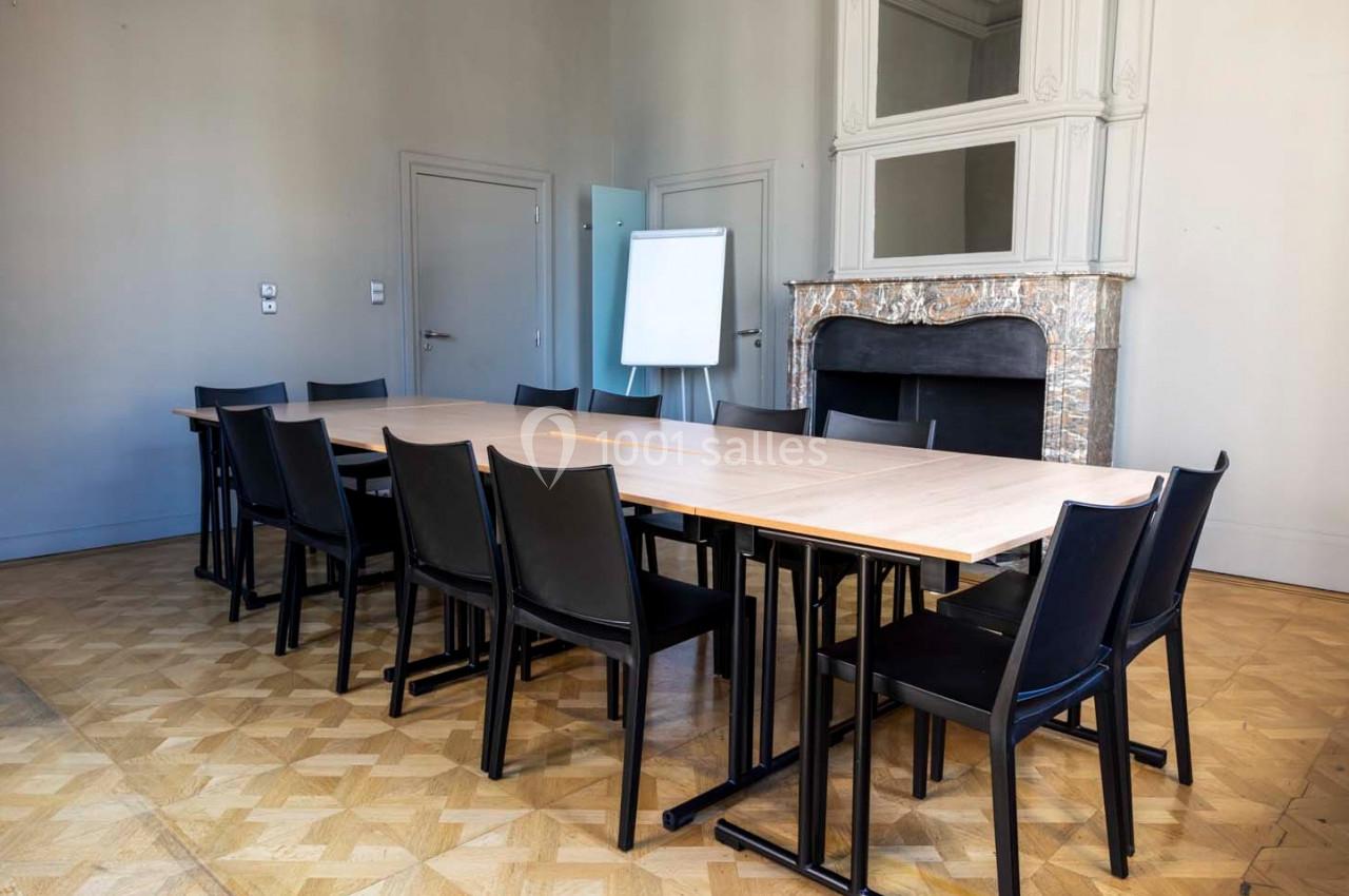 Salle de réunion avec une grande table en bois, des chaises noires, un tableau blanc et une cheminée décorative.