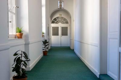 Couloir lumineux avec moquette verte, plantes en pot et portes blanches vitrées au fond.