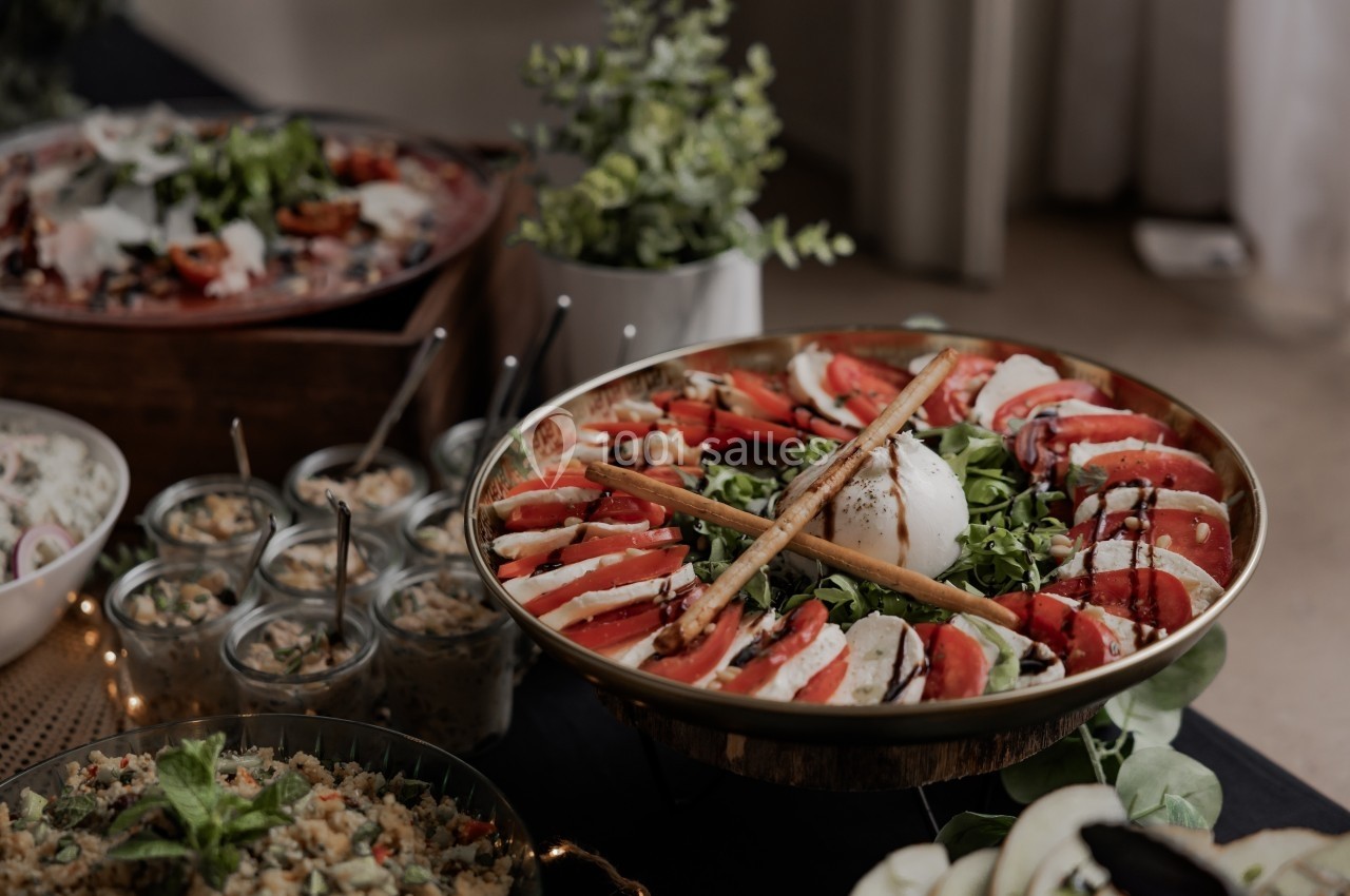 Assiette de salade caprese avec tomates, mozzarella, roquette et balsamique, entourée de plats variés sur une table.