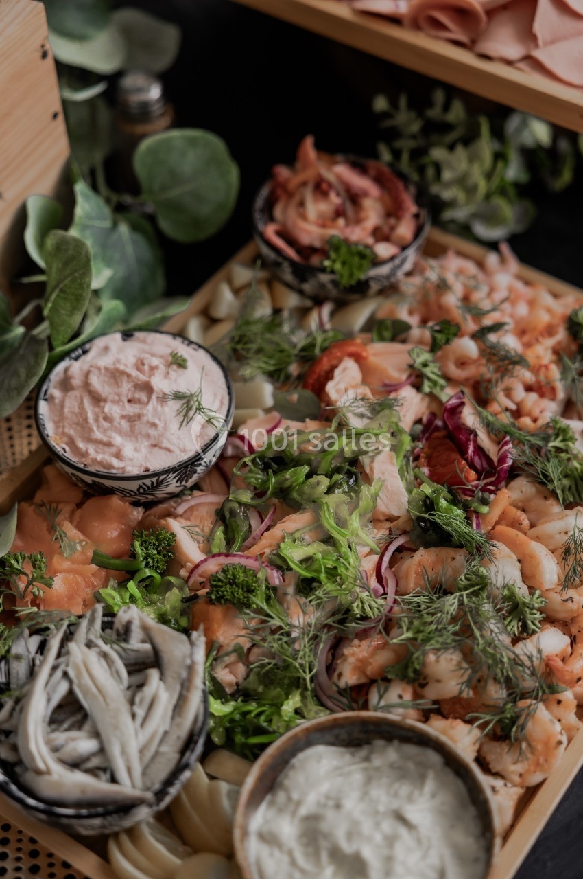 Plateau de fruits de mer avec crevettes, saumon, anchois, herbes fraîches et sauces variées, présenté sur un support en bois.