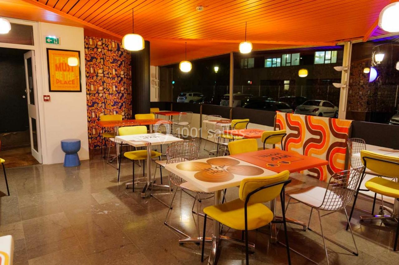 Salle de restaurant colorée avec des tables décorées, des chaises jaunes et un éclairage chaleureux.