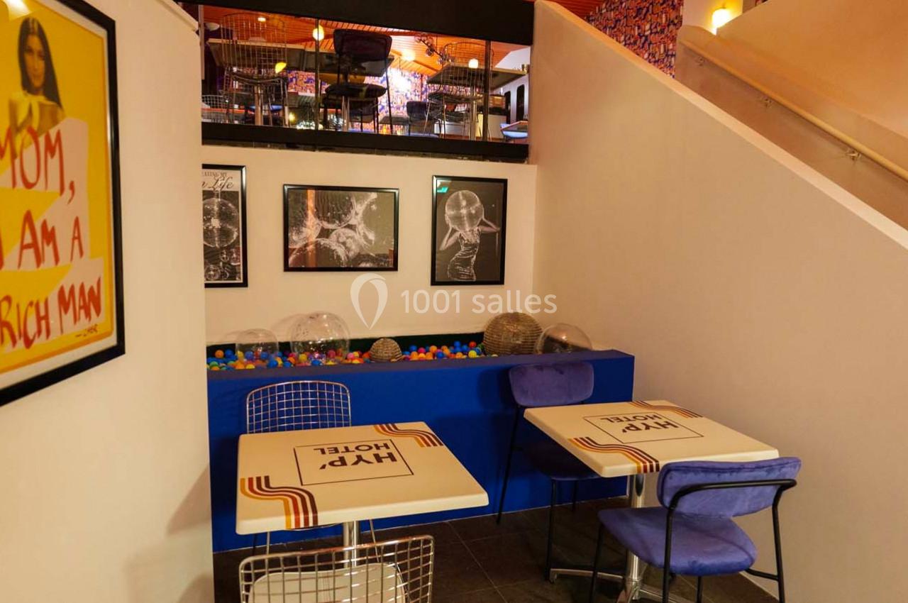 Deux tables avec chaises dans un café coloré, décoré de cadres, d'une affiche et d'une piscine à balles.