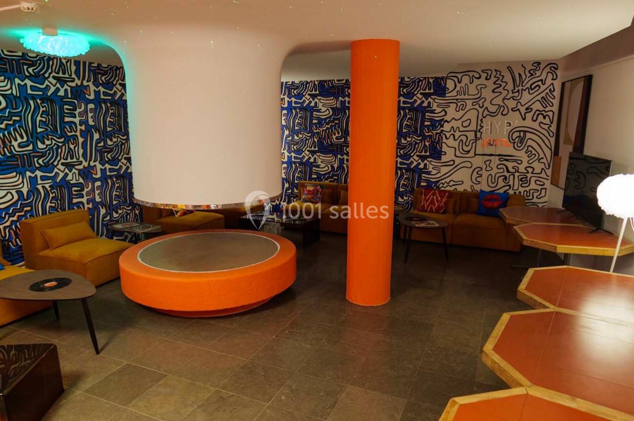 Salon coloré avec murs décorés de motifs abstraits, mobilier orange et jaune, et éclairage tamisé.