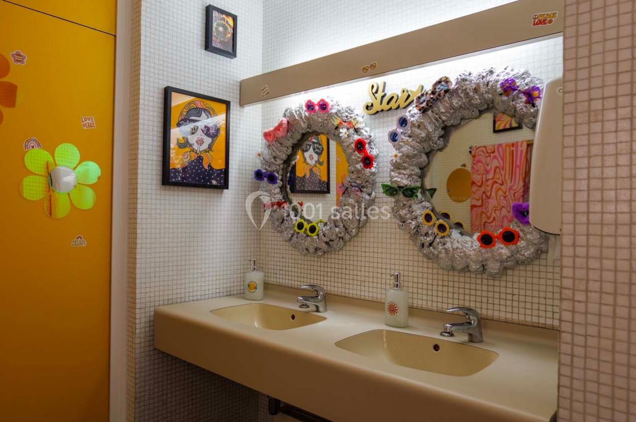 Deux lavabos avec miroirs décorés de couronnes colorées, entourés de cadres et d'un mur carrelé blanc.