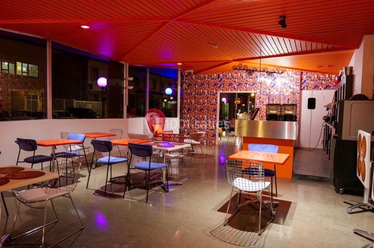 Salle de restaurant moderne avec des tables colorées, des chaises variées et un éclairage chaleureux en soirée.