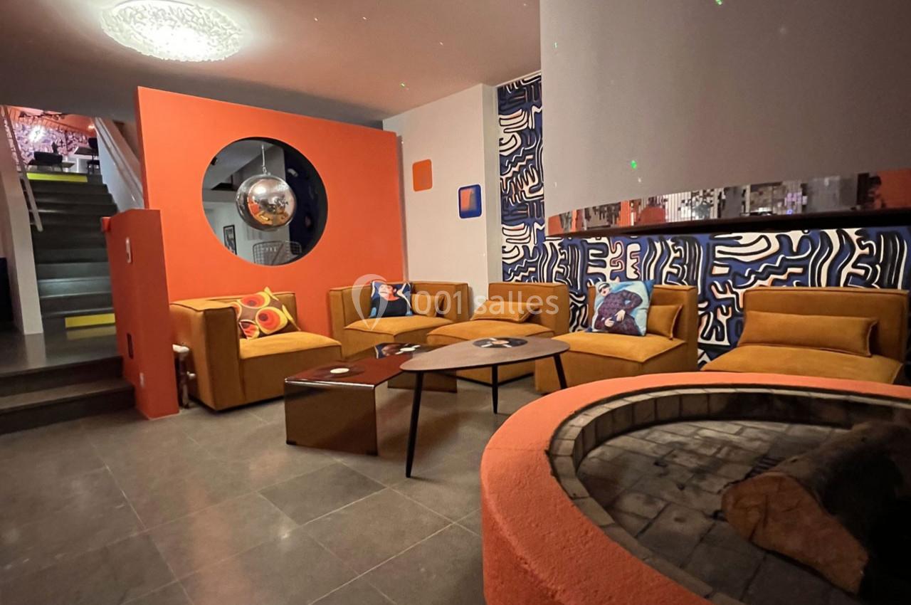 Salon moderne avec canapés orange, table basse, cheminée circulaire et décorations murales colorées.