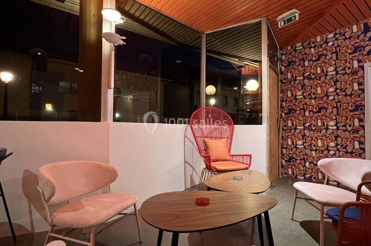 Espace intérieur avec mobilier coloré, chaises et tables, éclairé par des lampes et une grande baie vitrée donnant sur l…