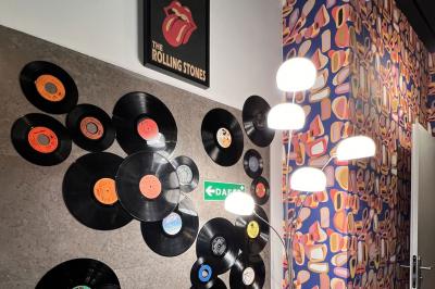 Mur décoré de vinyles, panneau des Rolling Stones et lampes modernes, avec un papier peint coloré en arrière-plan.