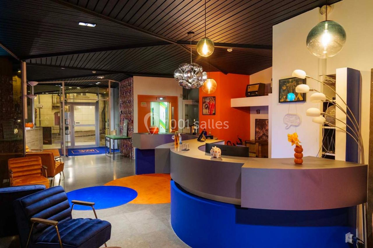 Intérieur d'un hall d'accueil moderne avec comptoir arrondi, fauteuils, décorations colorées et éclairage design.