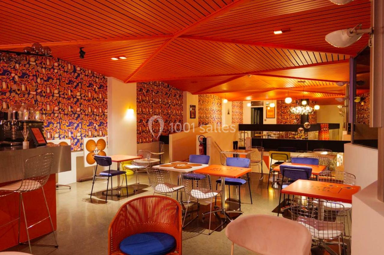 Salle de restaurant colorée avec des murs ornés de motifs vifs, des tables orange et des chaises modernes.