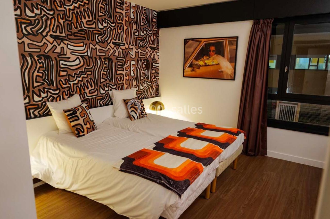 Chambre avec deux lits simples, décorée de motifs géométriques colorés et éclairée par une lampe de chevet dorée.