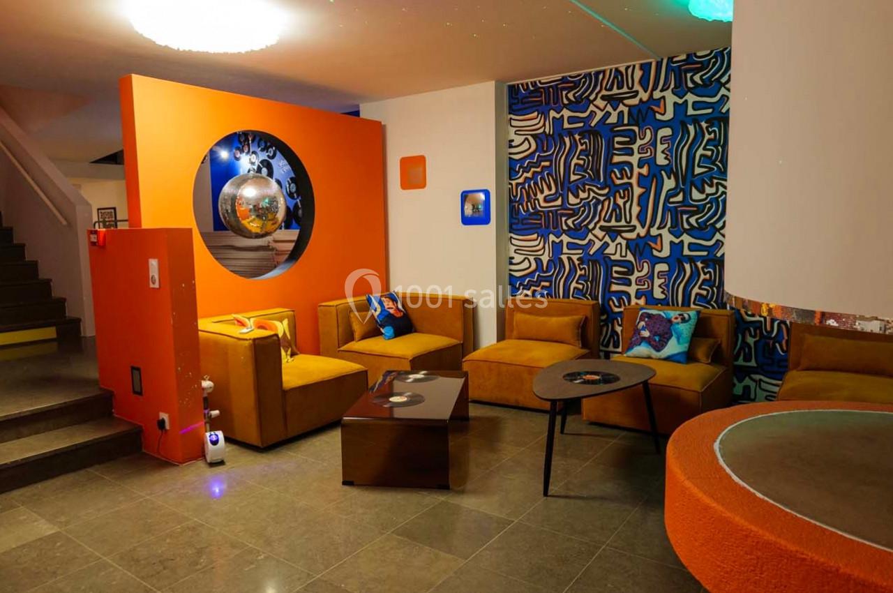 Espace salon coloré avec canapés orange, tables basses et décorations murales artistiques dans un intérieur moderne.