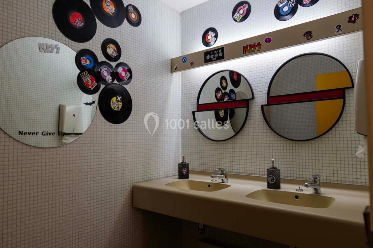 Salle de bain décorée avec des disques vinyles sur les murs, deux lavabos et miroirs ronds au-dessus.