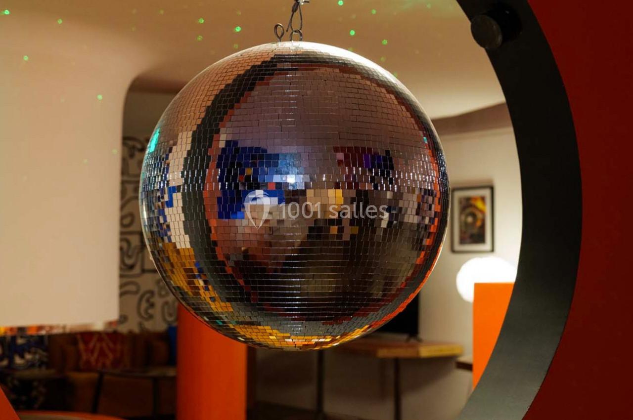 Boule à facettes suspendue dans une pièce aux tons chauds, reflétant des lumières et des éléments environnants.