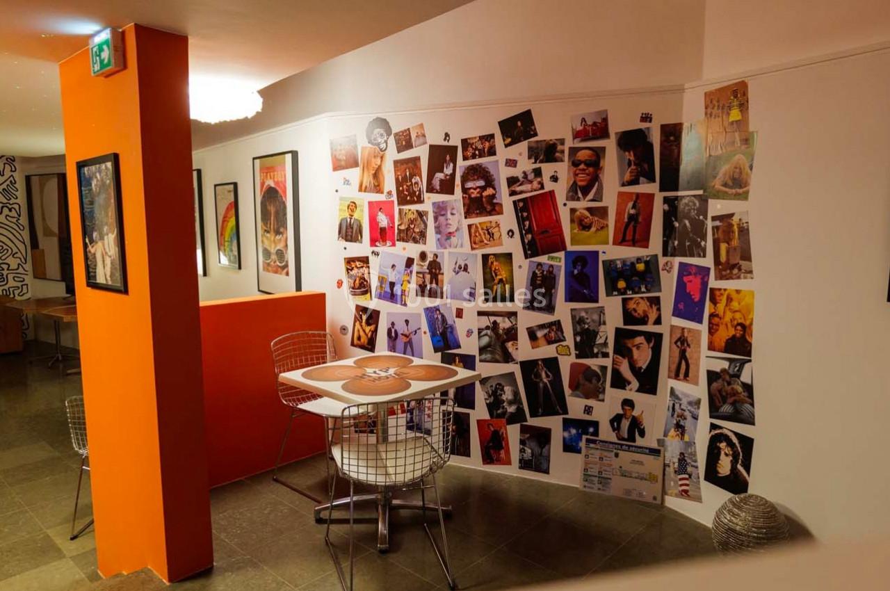 Mur décoré de nombreuses affiches et illustrations colorées dans un espace intérieur avec table et chaises modernes.