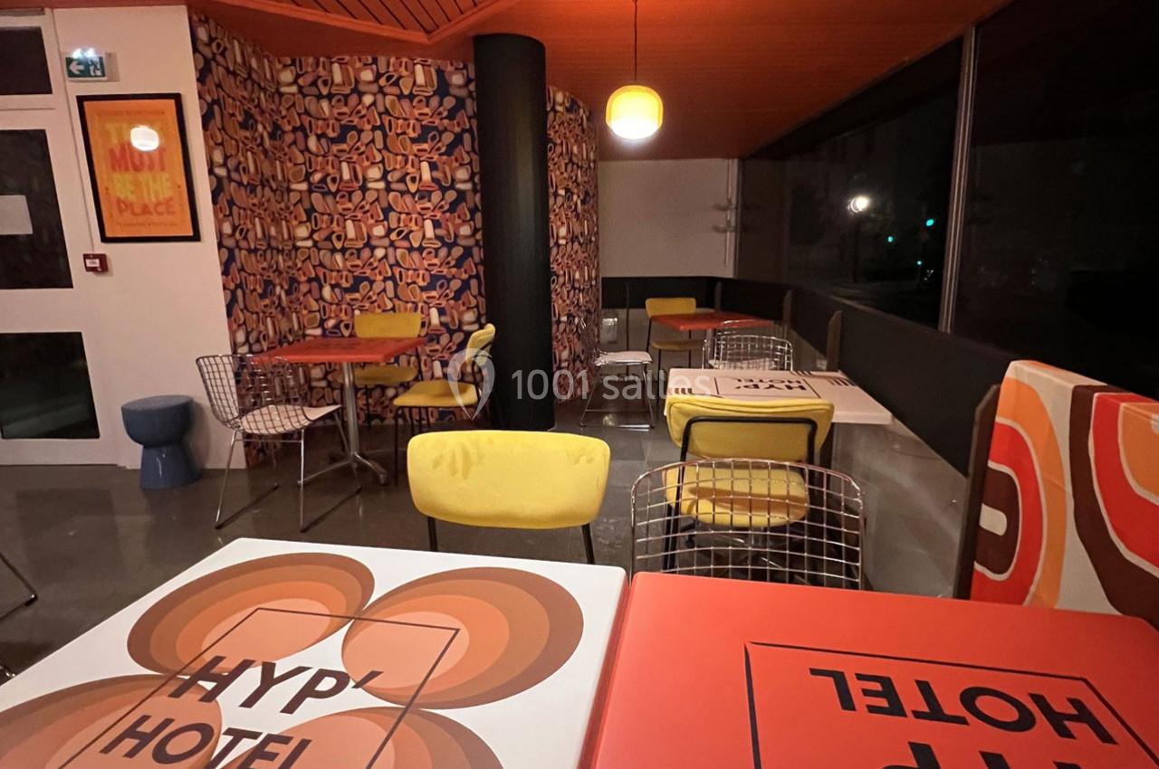 Salle de restaurant colorée avec tables décorées, chaises design, éclairage chaleureux et grandes baies vitrées.