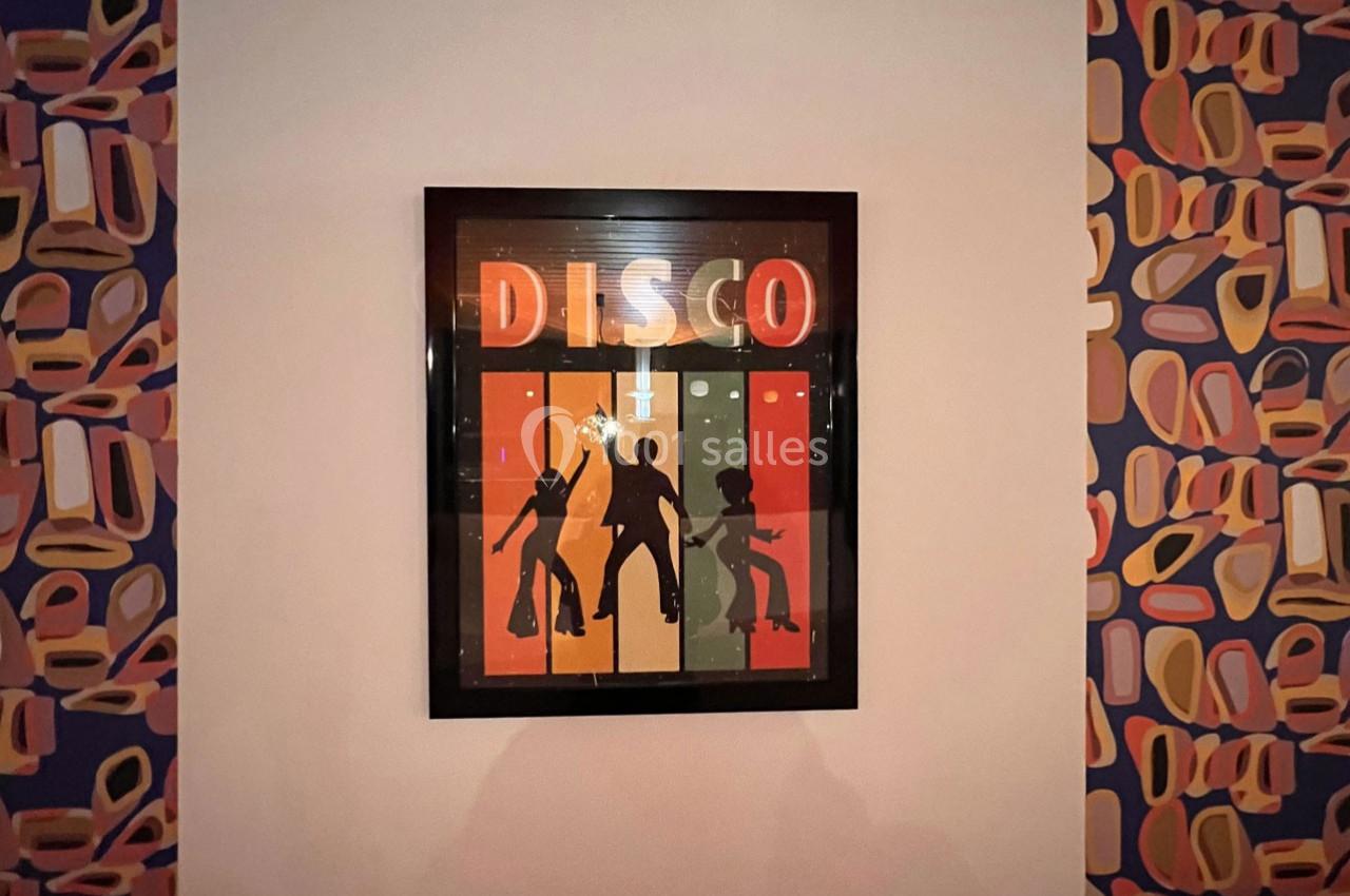 Affiche encadrée avec le mot ’DISCO’ et des silhouettes dansantes sur un fond coloré, accrochée à un mur décoré.